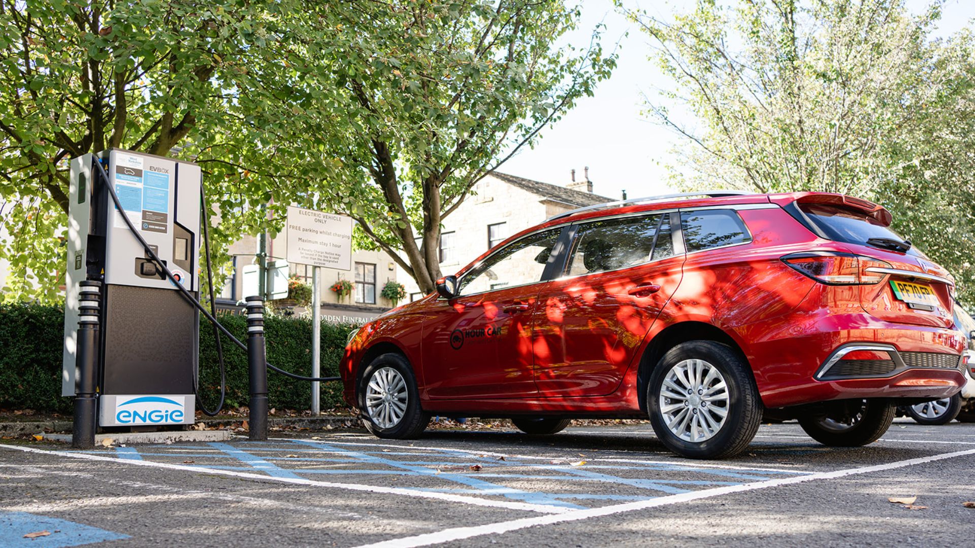A red electric car, plugged into a charger whilst parked in a bay