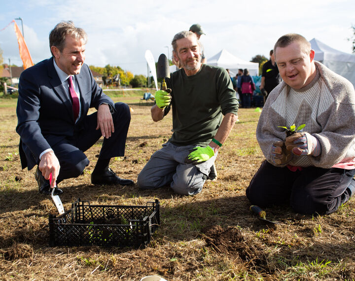 The Metro Mayor Dan Norris and two members of the public are kneeling in a field holding trowels and plug plants ready to plant into the ground.